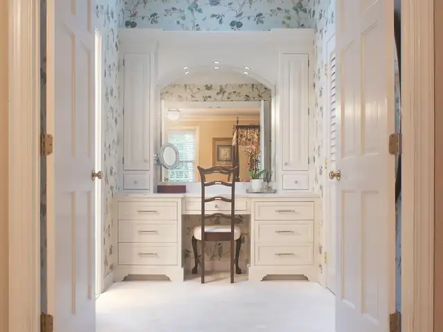 Bathroom dressing area with a white built-in vanity desk, arched mirror and botanical wallpaper