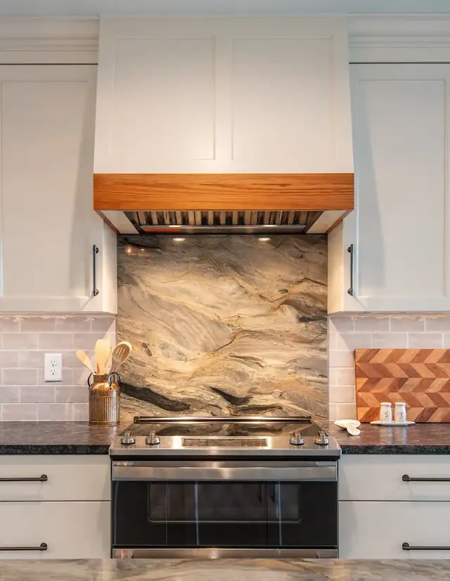 Range wall with a white hood trimmed in wood, a dramatic stone slab backsplash and herringbone tile accents