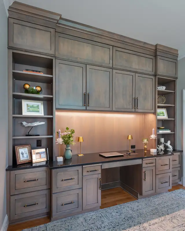 Built-in home office in Tarrington with gray-stained cabinetry, open shelves, a desk with under-cabinet lighting and a black counter
