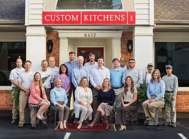 The Custom Kitchens team gathered in front of the red Custom Kitchens sign at 6412 Horsepen Road